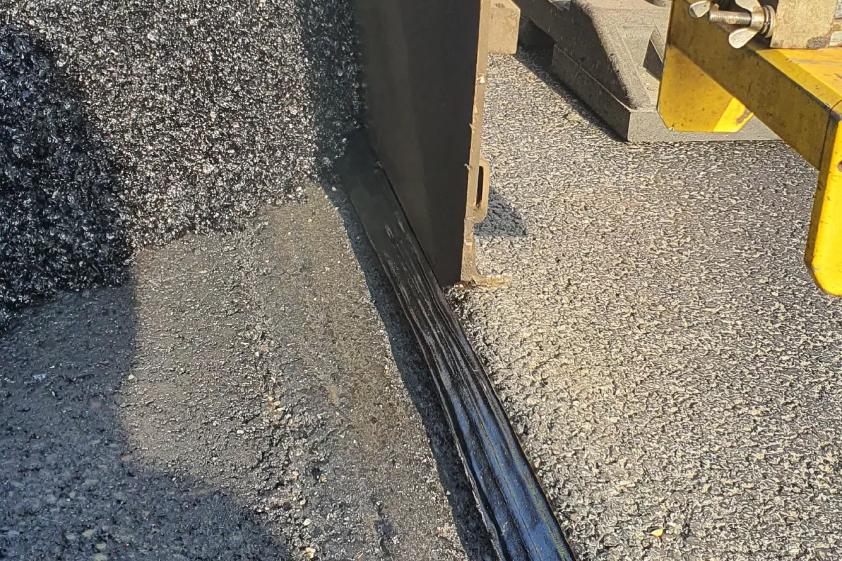 The paver working along the edge of the adjacent lane.